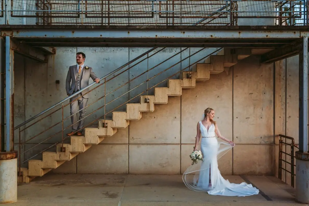 Groom on an industrial steel staircase above Beth in her fitted gown, Almyra, Paphos