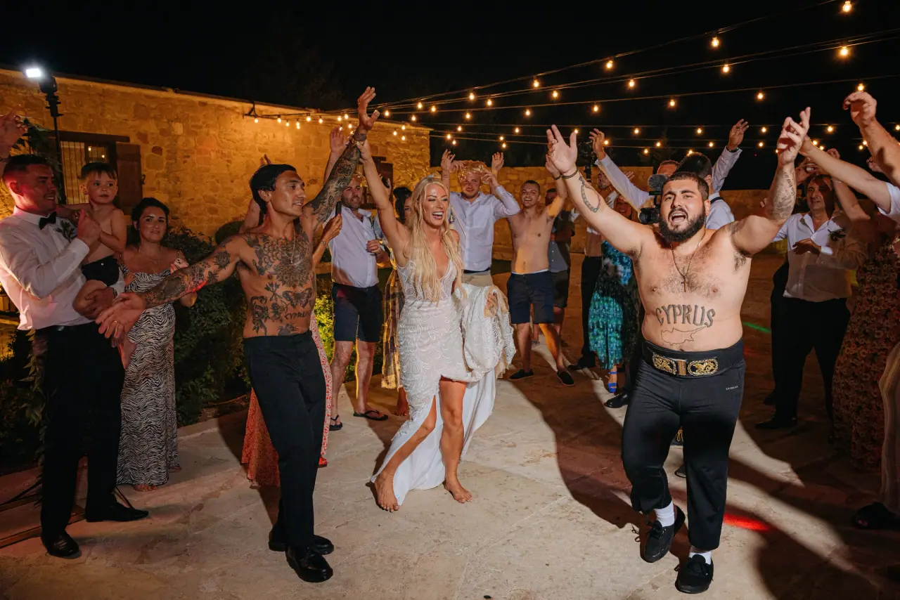 Shirtless guests dancing with the bride under festoon lights at Liopetro, Kouklia