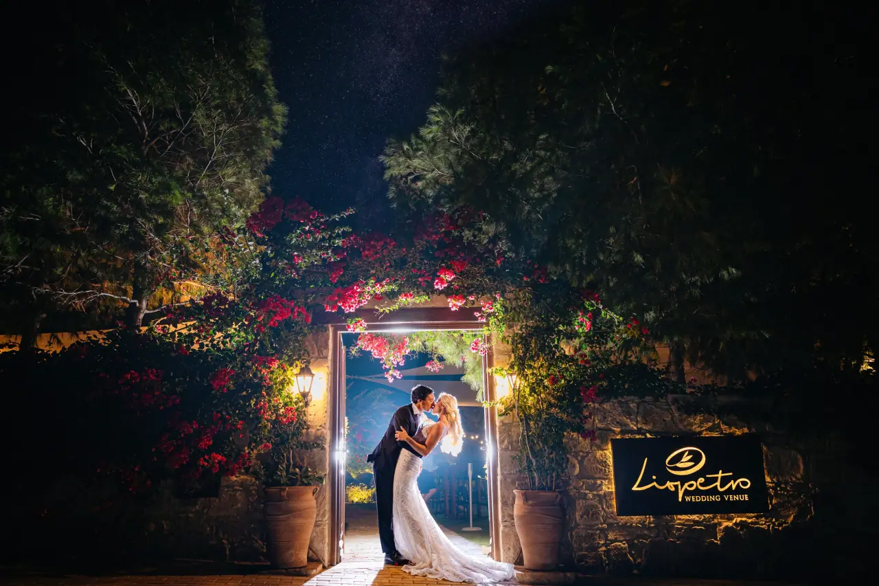 Emma and Aaron kissing in a lit, bougainvillea-framed doorway at night at Liopetro, Kouklia