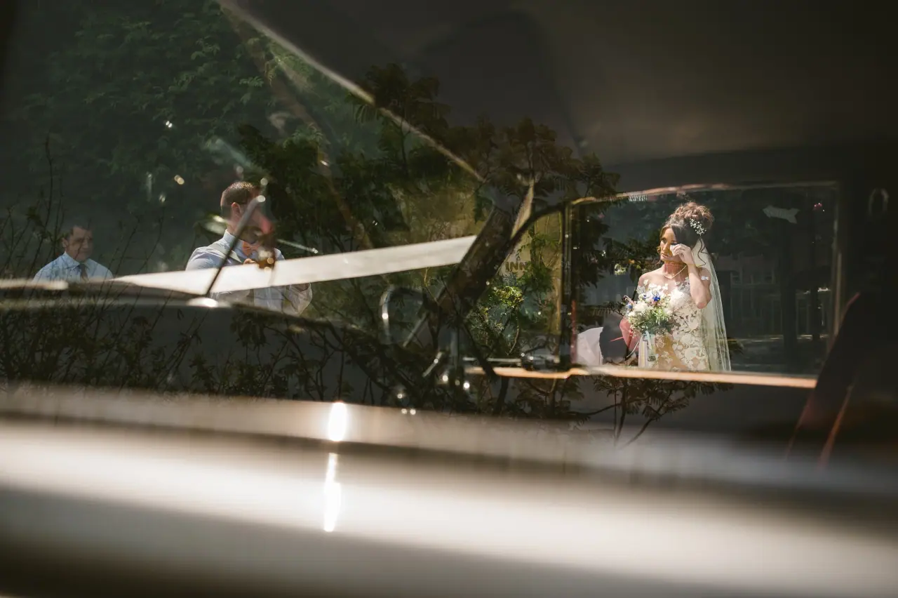 Bride glimpsed through the windscreen of a vintage car, reflections across the glass