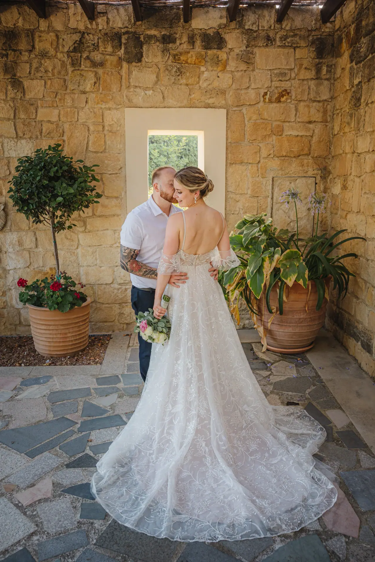 Groom helping his bride in a stone courtyard with potted plants, Aphrodite Hills
