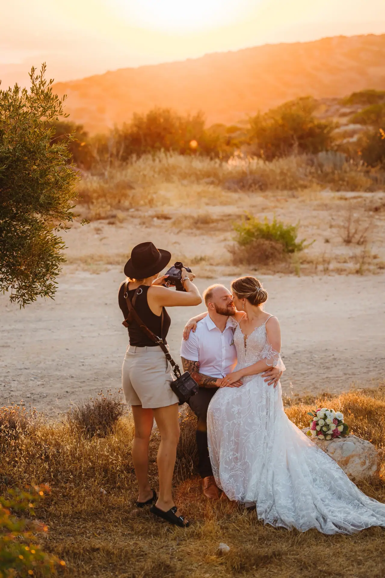 Photographer in a hat capturing a seated bride and groom at golden hour, Aphrodite Hills