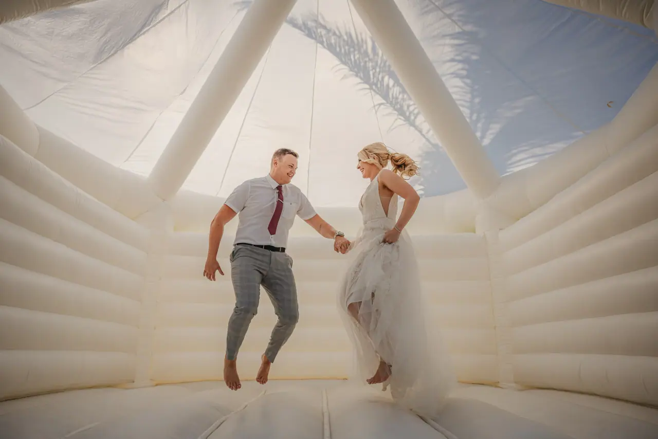 Sarah and Aiden jumping hand in hand in a white bouncy castle at Alassos