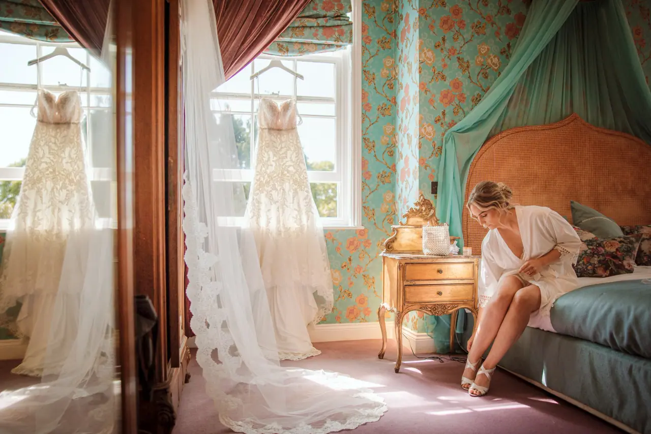 Olivia getting ready in an ornate bedroom, her gown and veil hanging by the window