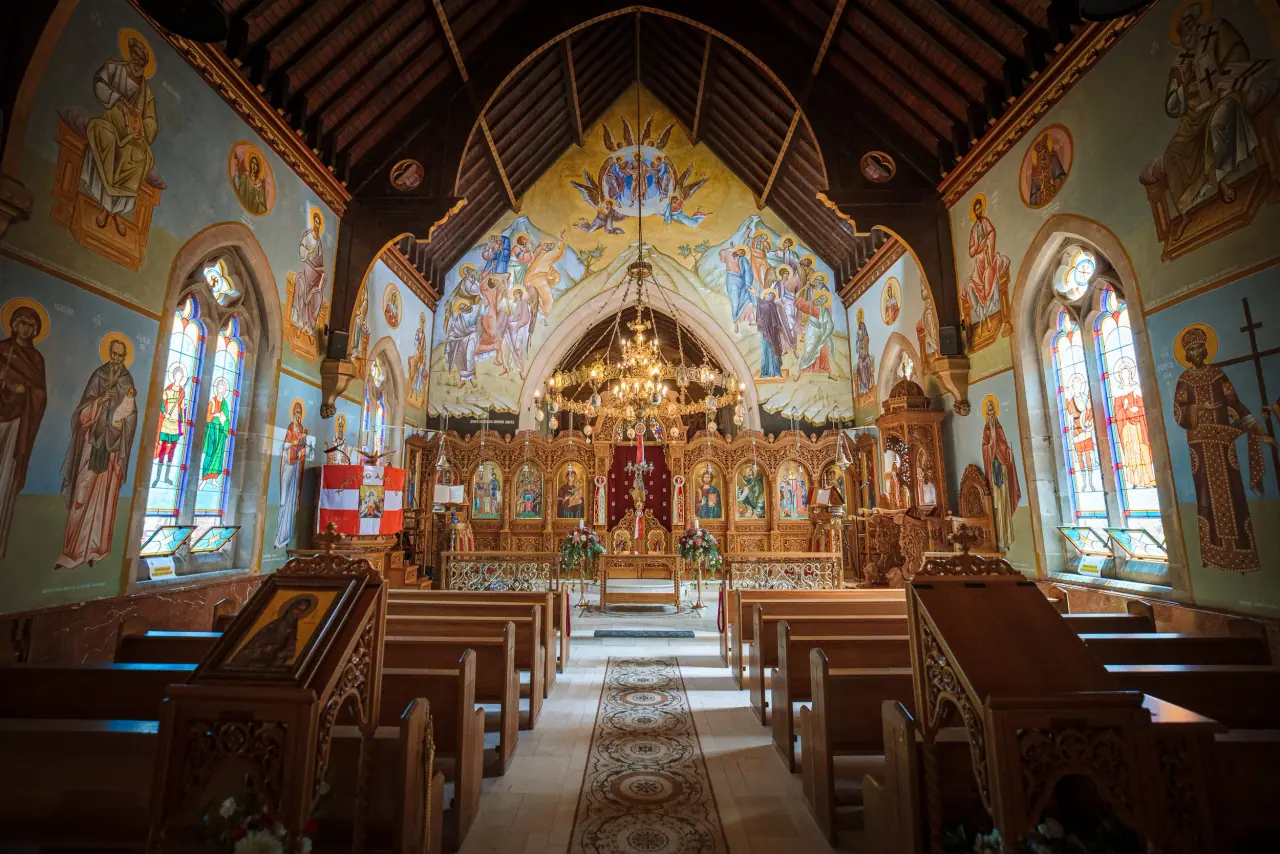 Frescoed Orthodox church interior with wooden pews and a gilded iconostasis