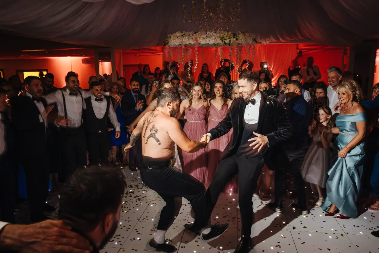 Groom dancing with a shirtless guest as the crowd cheers