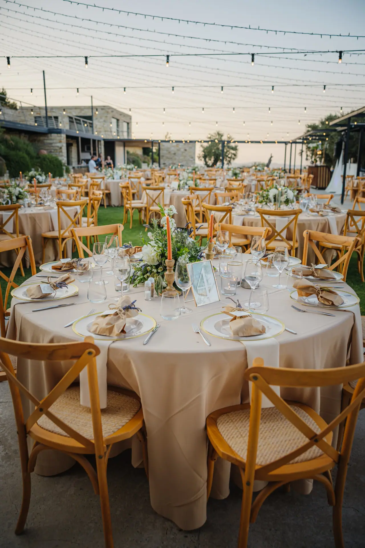 Round tables in cream linen with wooden chairs set outdoors under festoon lights at Dafermou