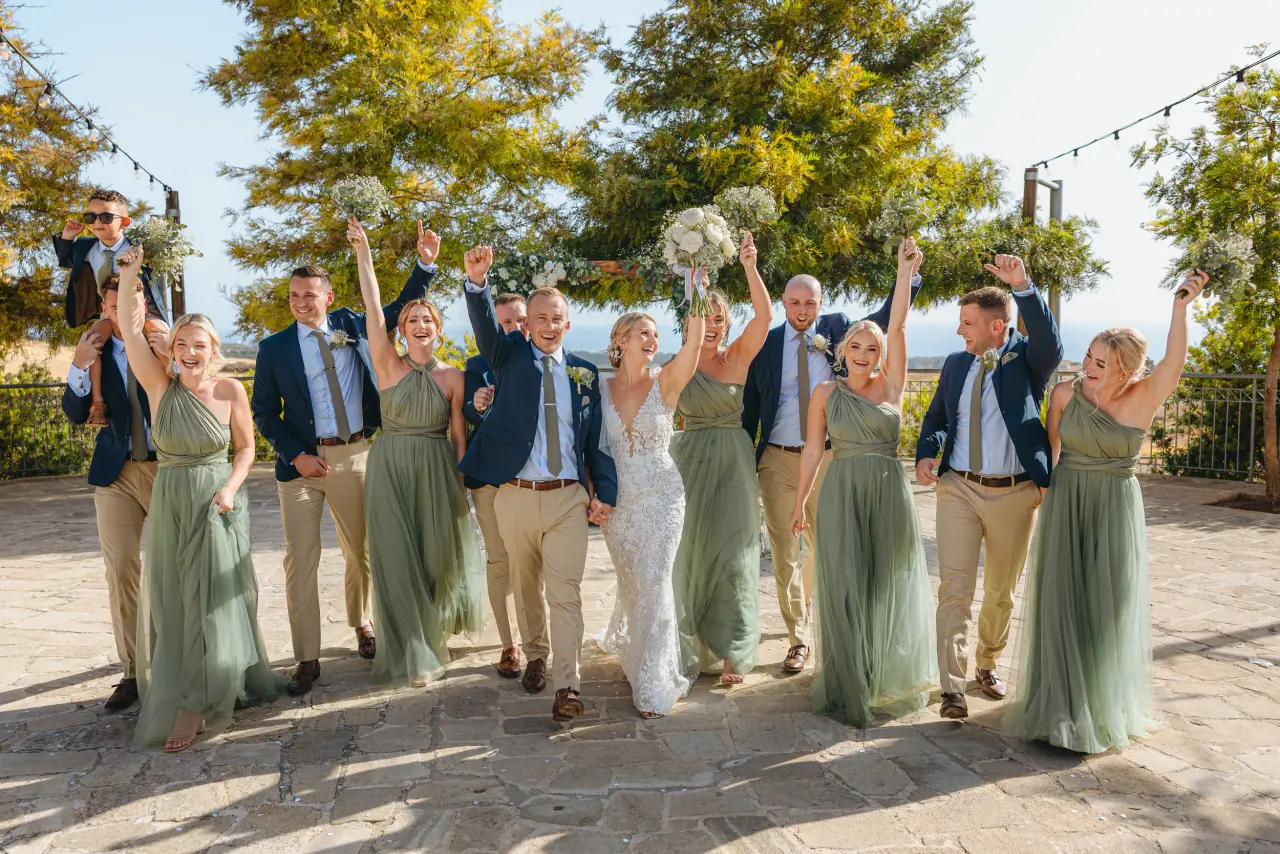 Beth and Josh's bridal party in sage green and navy cheering with arms raised at Liopetro