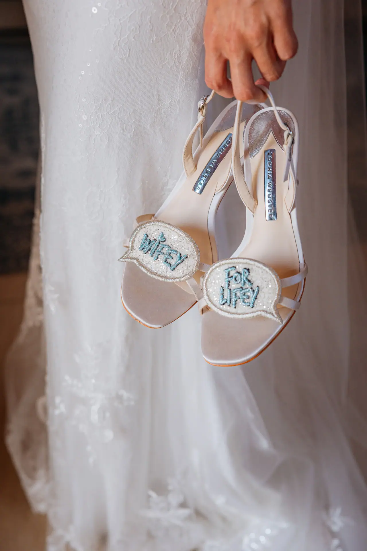 Abby holding her 'Wifey For Lifey' sandals beside her lace gown