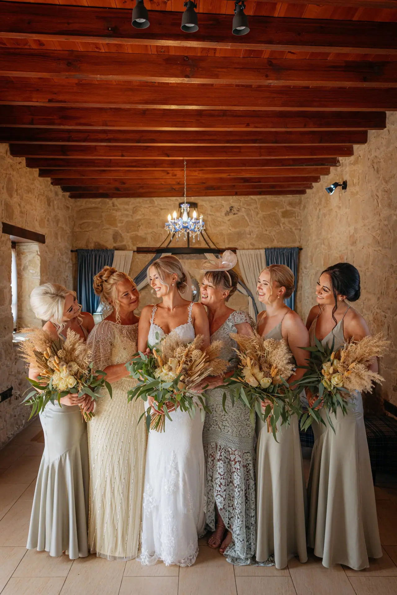 Bridesmaids in sage dresses holding dried-flower bouquets in a beamed stone room, Liopetro