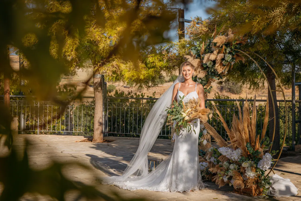 Abby in her gown and veil beside a dried-flower ceremony arch at Liopetro