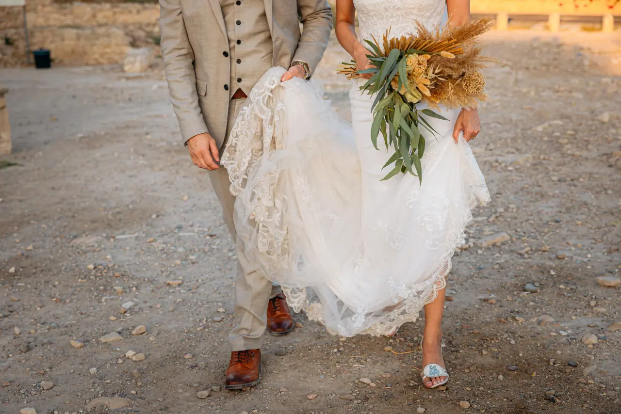 Bride lifting her hem as the couple walks across dusty ground with her bouquet