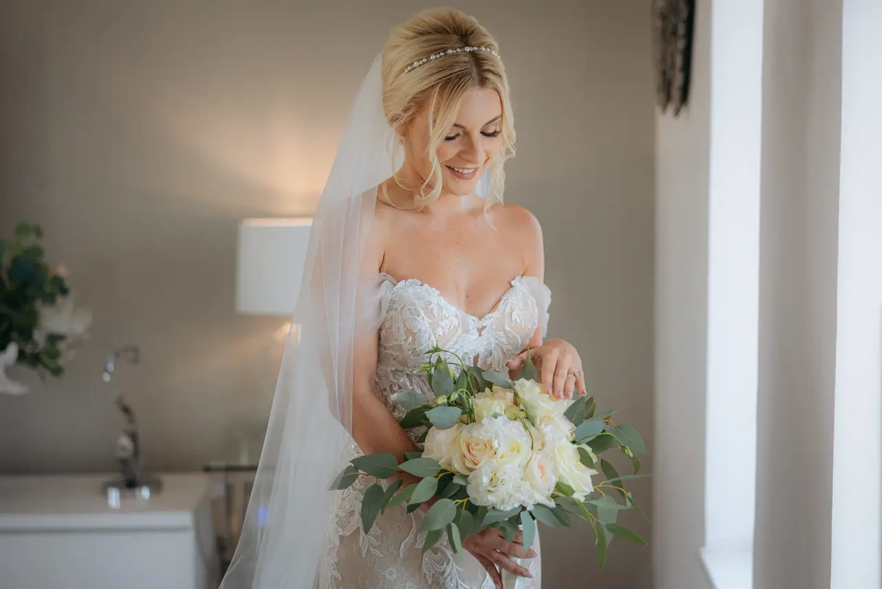 Amy holding her white rose bouquet in the bedroom at Alassos