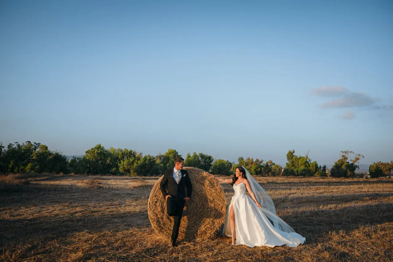 Amy and Lee beside a round hay bale in a field at golden hour