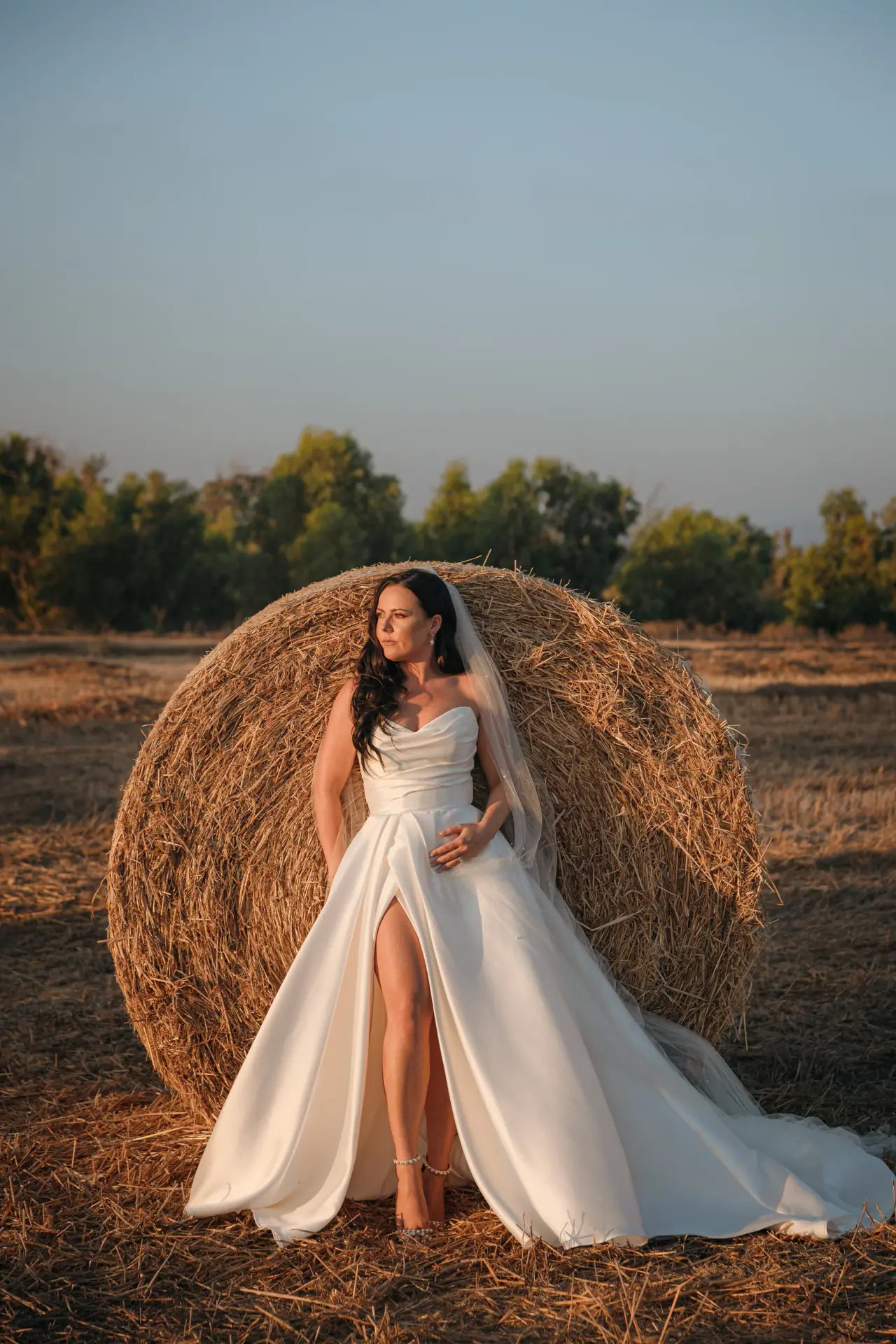 Amy posing against a round hay bale in her gown with a thigh-high slit