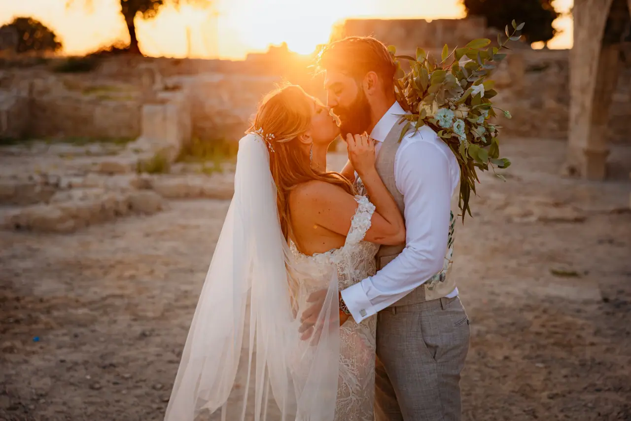 Annie and Iain kissing at sunset among stone ruins, groom holding the bouquet