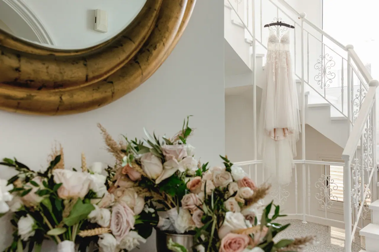 Pink rose bouquet before a gold mirror with the dress hanging on a white staircase, Coral Residence