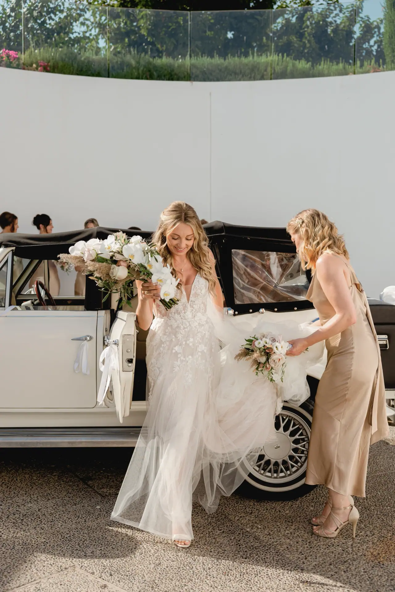 Becky and a bridesmaid beside a vintage white wedding car