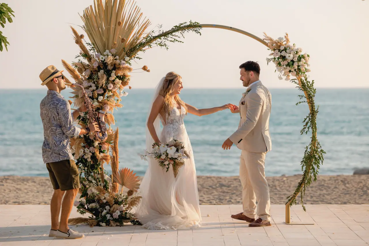 Becky and Dan exchanging vows beneath a dried-flower arch by the sea at Coral Residence