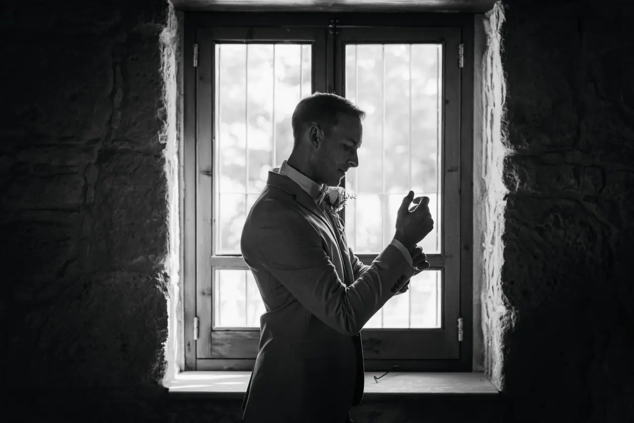 Black-and-white silhouette of Lewis fastening his cufflinks at a window