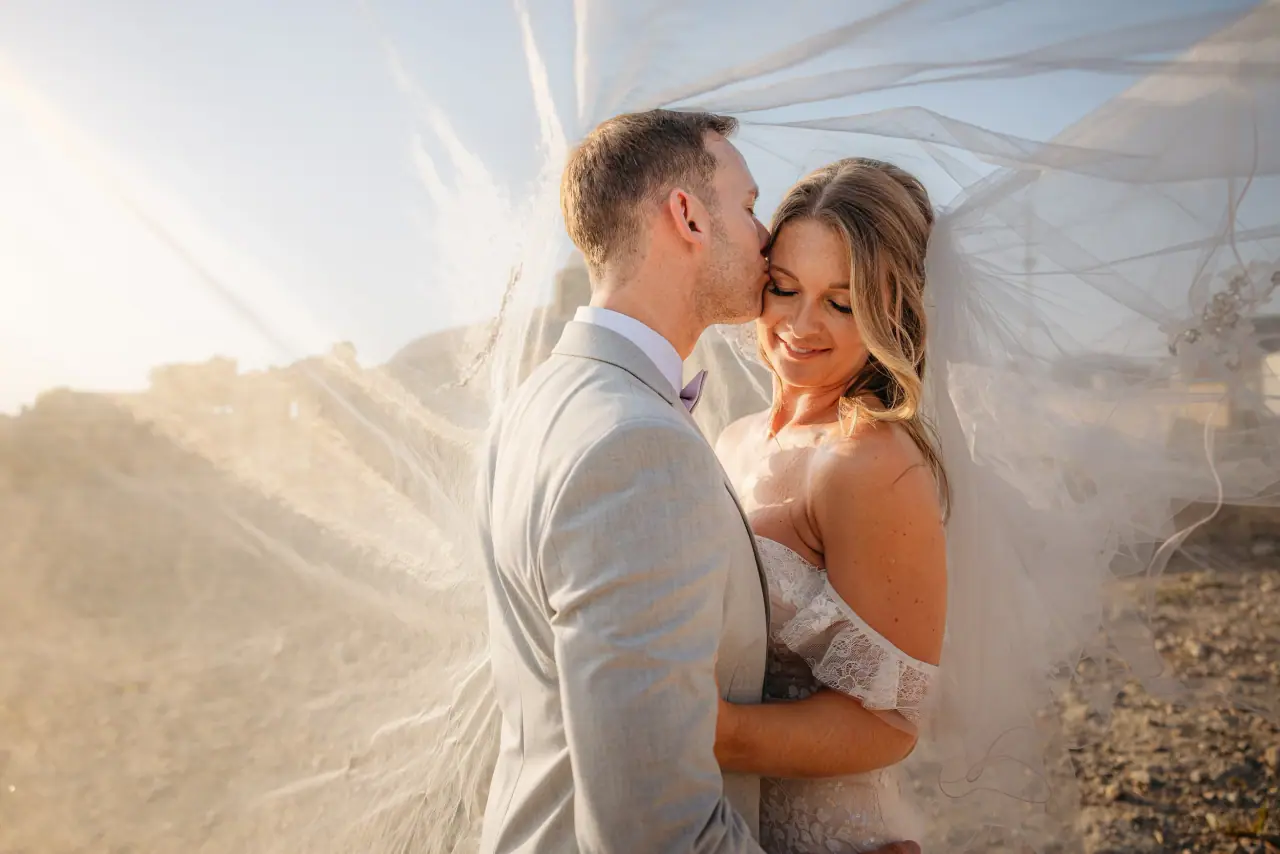 Lewis kissing Laura's forehead beneath her sunlit veil at Liopetro
