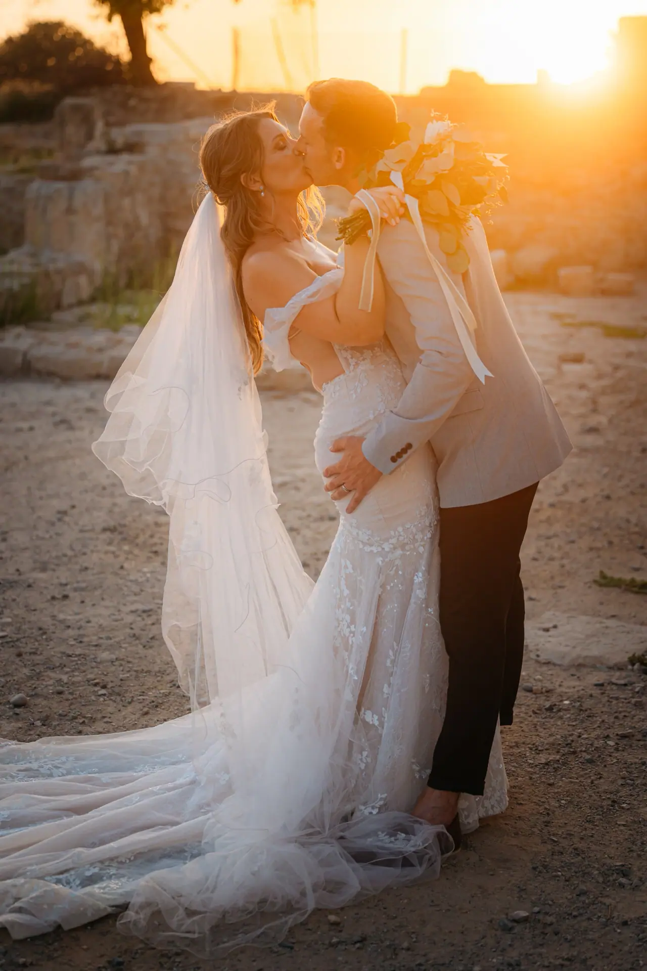 Laura and Lewis kissing at golden hour among ruins, her long veil trailing, Liopetro