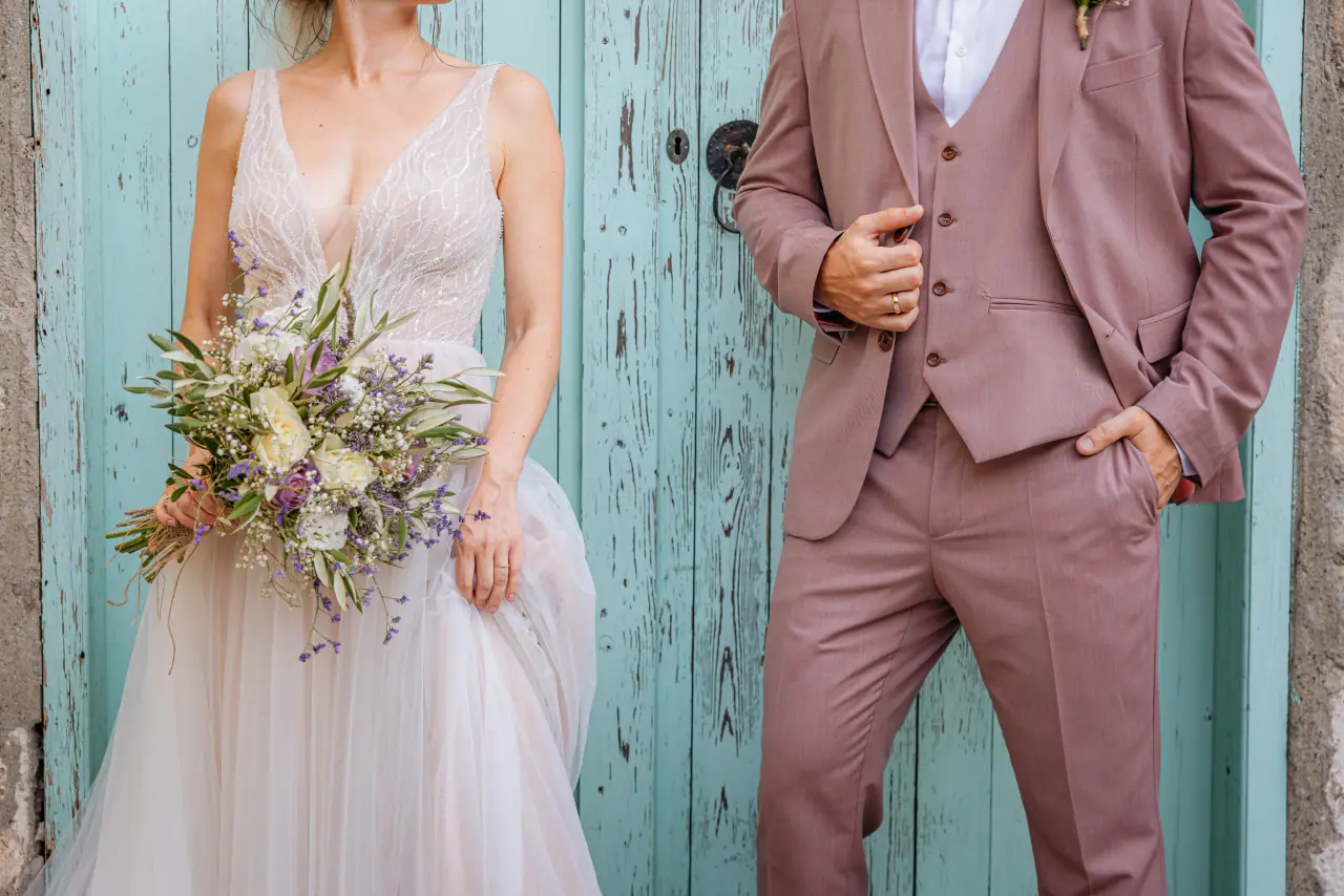 Bride with a wildflower bouquet beside the groom in a dusky pink suit at a turquoise door