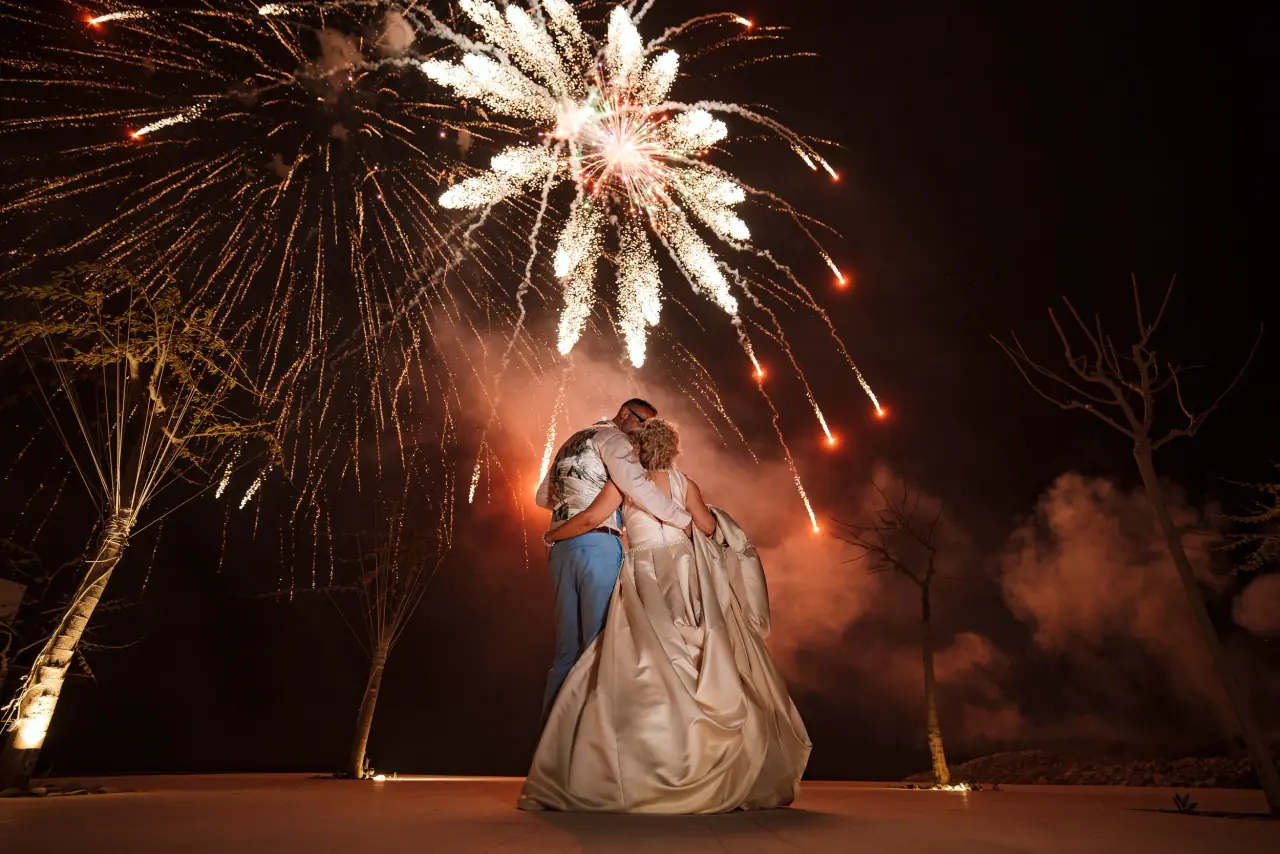 Debz and Richard embracing as fireworks burst overhead at night