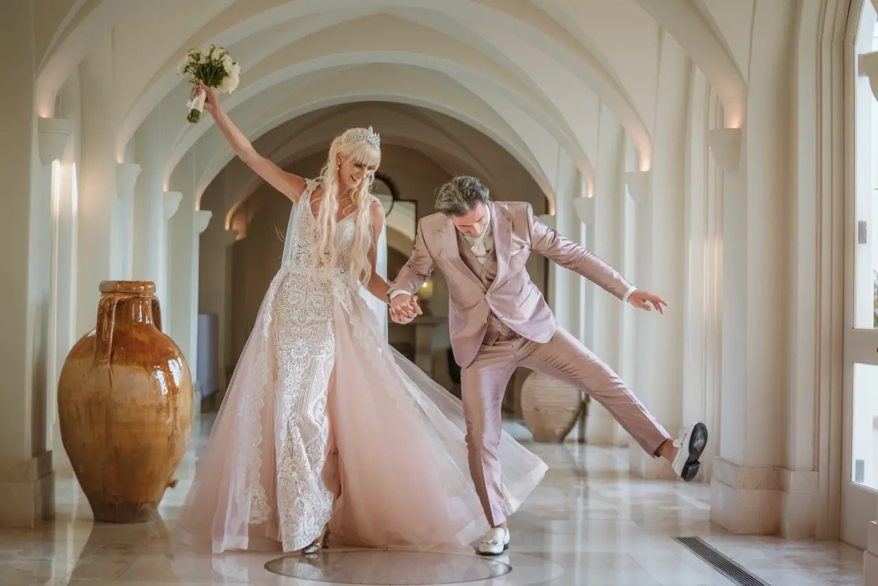Disa and John dancing playfully in a white arched corridor at Anassa