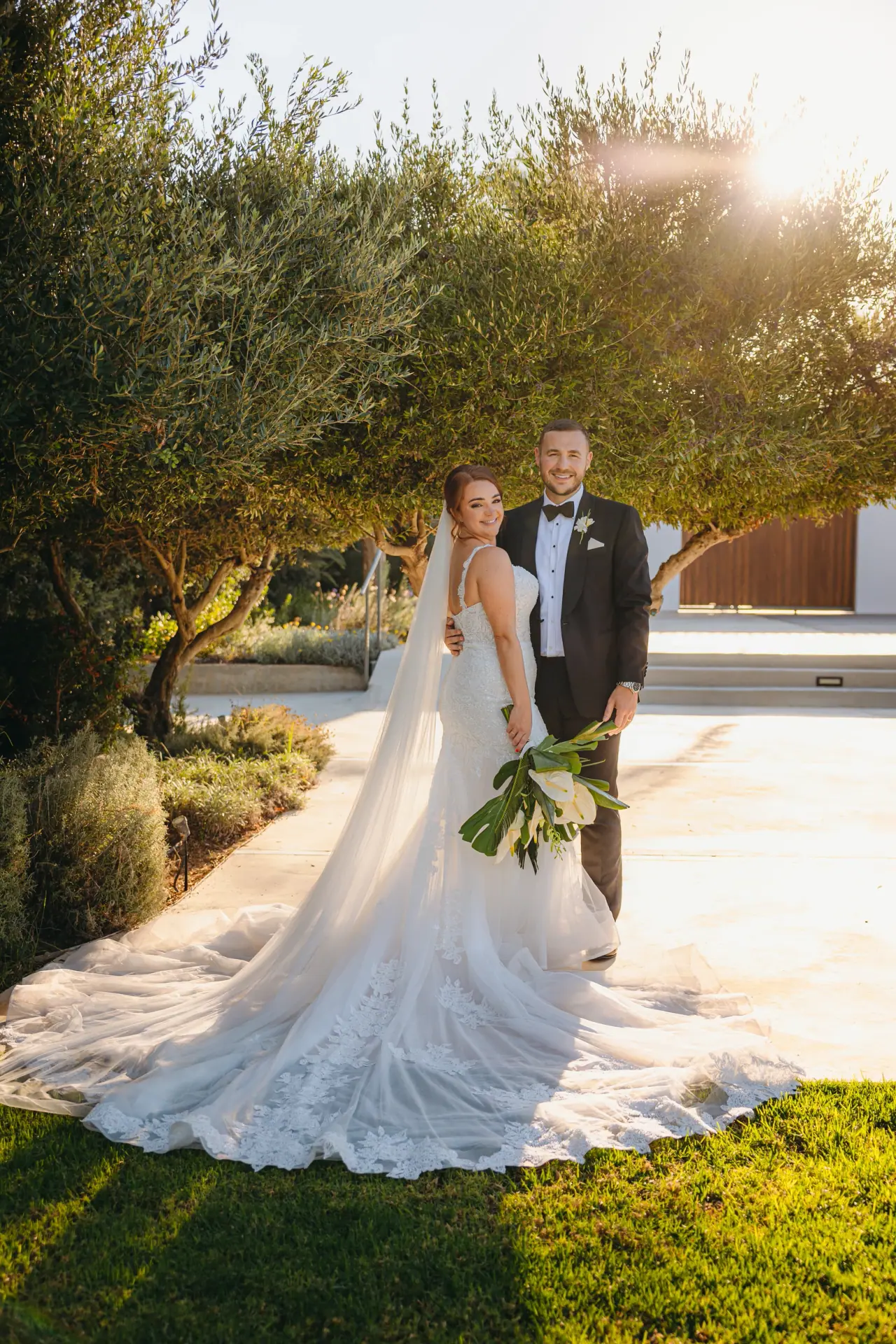 Emma and Denis on a lawn among olive trees, her long train spread, Alassos