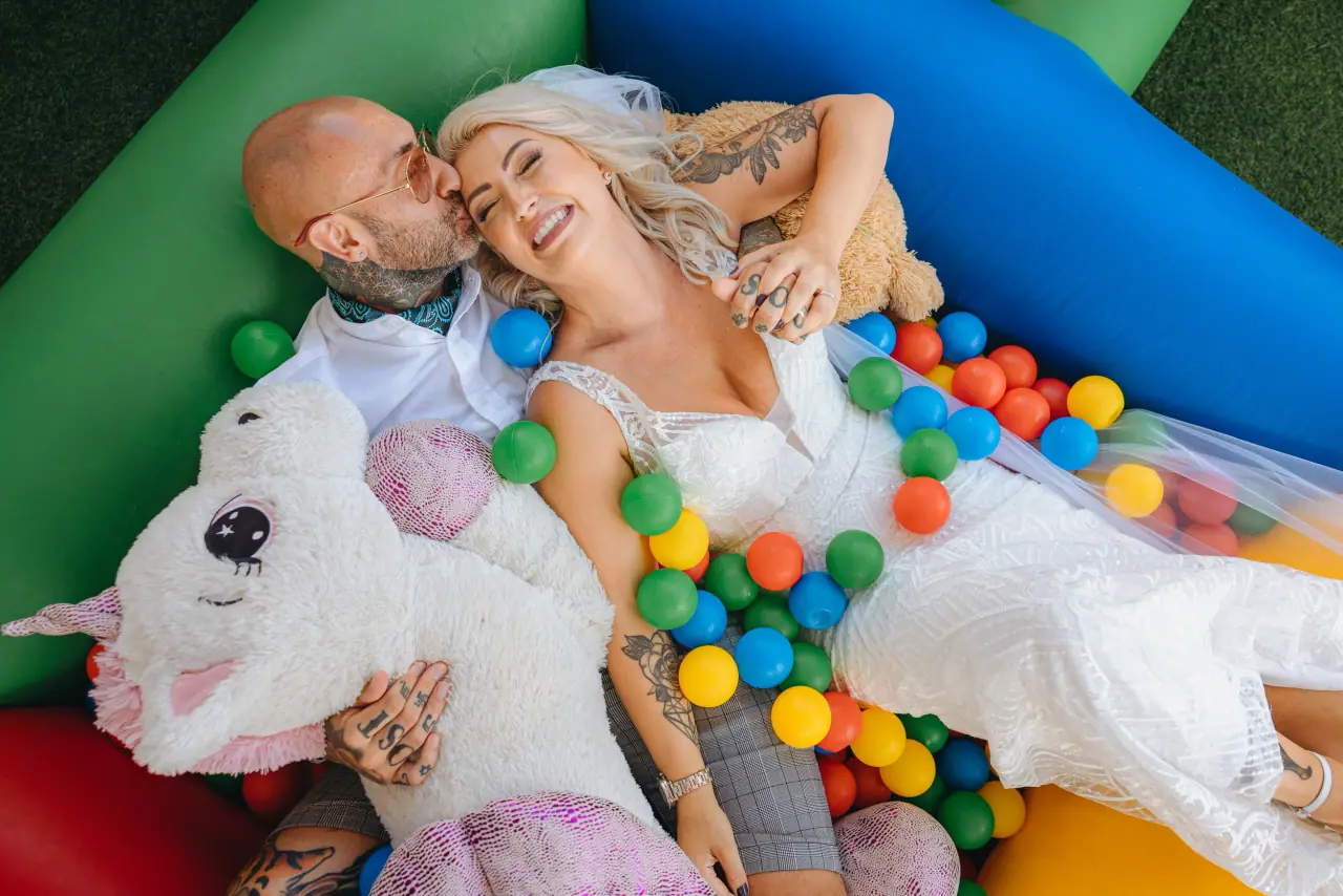 Tattooed bride and groom lying in a colourful ball pit with a plush toy