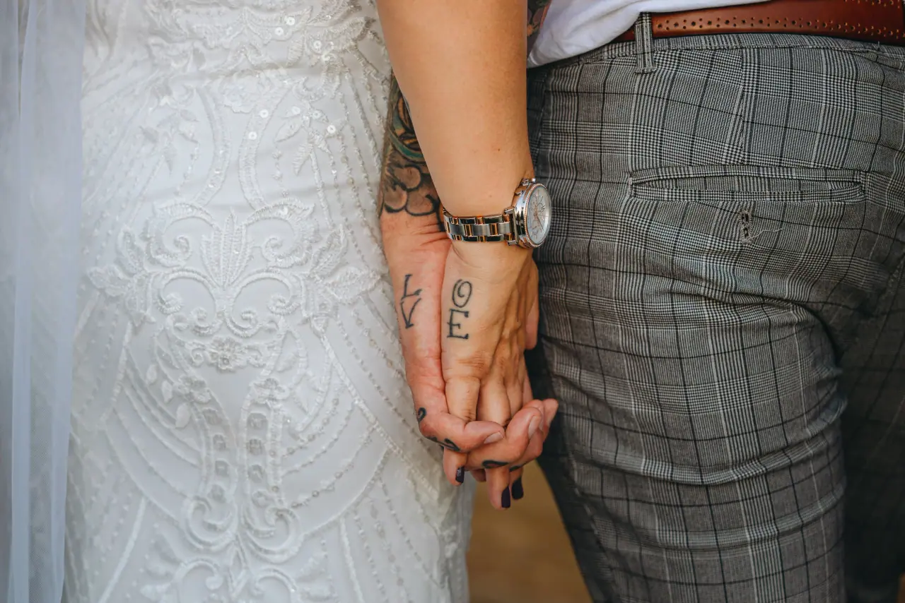 Close-up of tattooed hands held together against the bride's lace dress