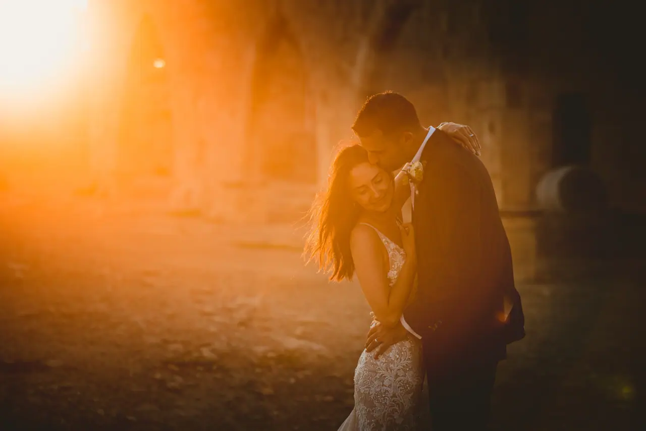 Kayleigh and Ryan embracing in golden backlight among ruins