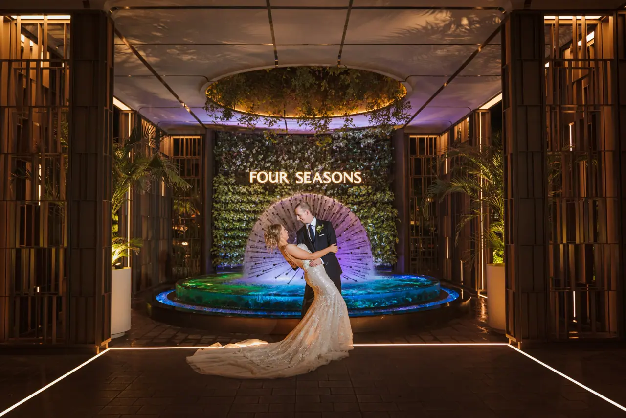 Mark and Candice kissing before a lit fountain and Four Seasons green wall, Limassol