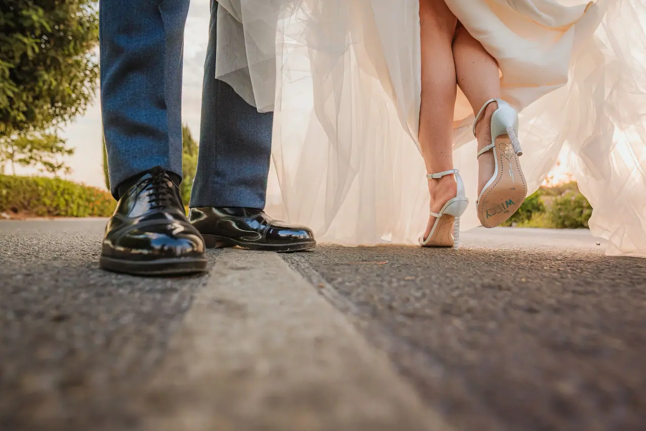 Low view of the groom's polished shoes and bride's heels stepping across a road
