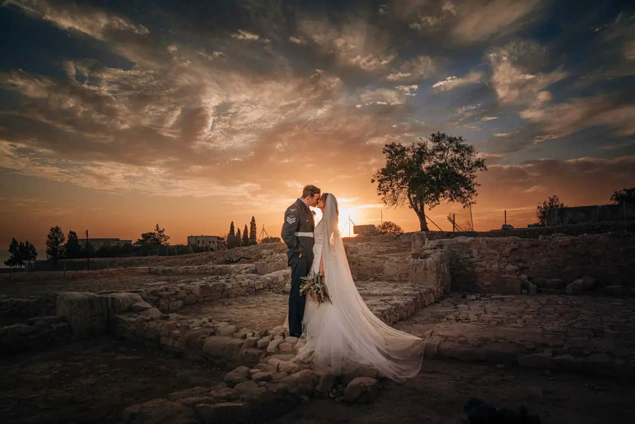 Michelle and Lewis kissing beside a lone tree beneath a dramatic sunset sky, Liopetro