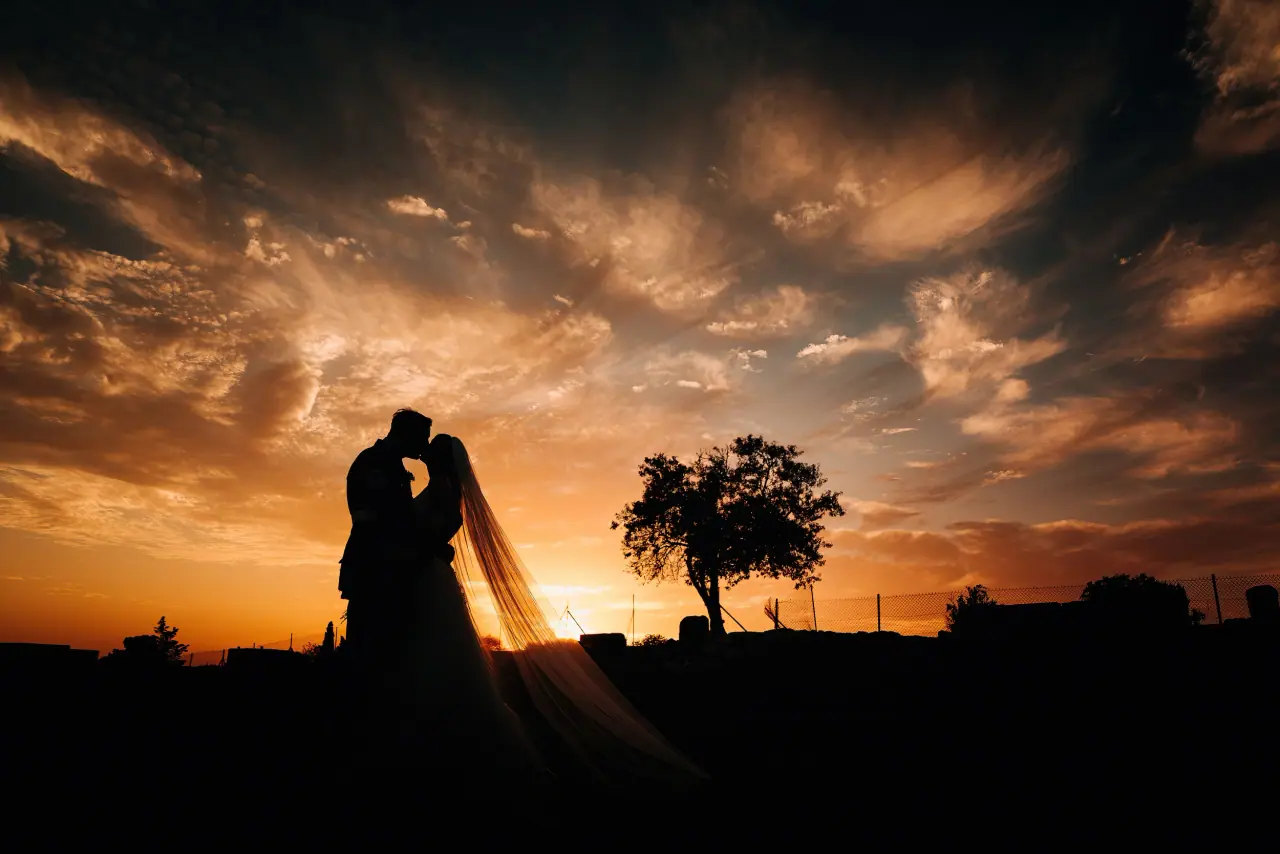 Michelle and Lewis silhouetted in a kiss beneath dramatic sunset clouds