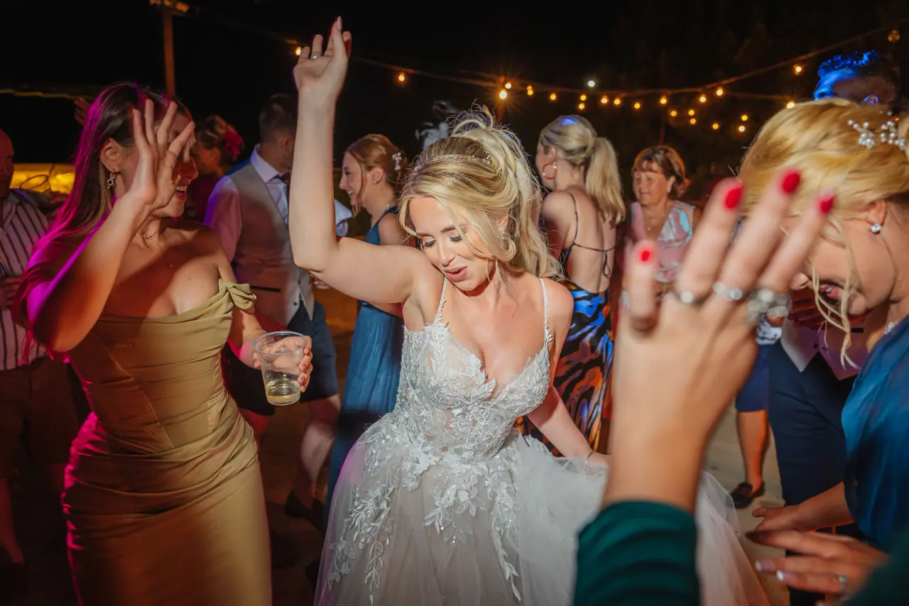 Bride dancing with arms raised among guests at night at Liopetro