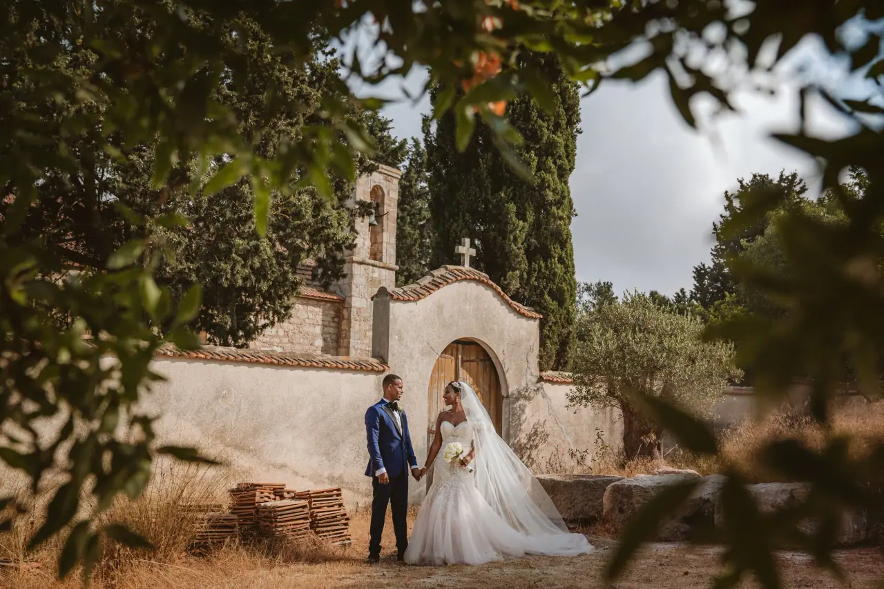 Daniel and Kayleigh before a small whitewashed chapel framed by trees at Minthis Hills
