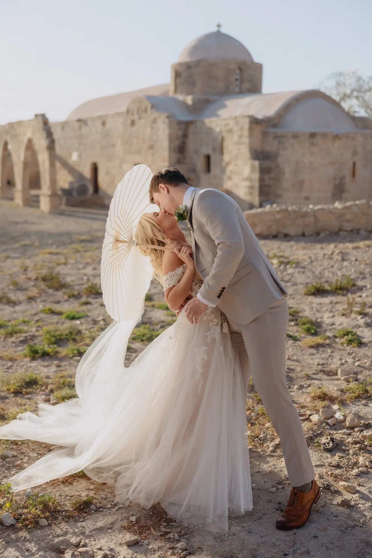 Bride and groom kissing beneath a parasol beside ancient ruins at Liopetro, Kouklia, Paphos