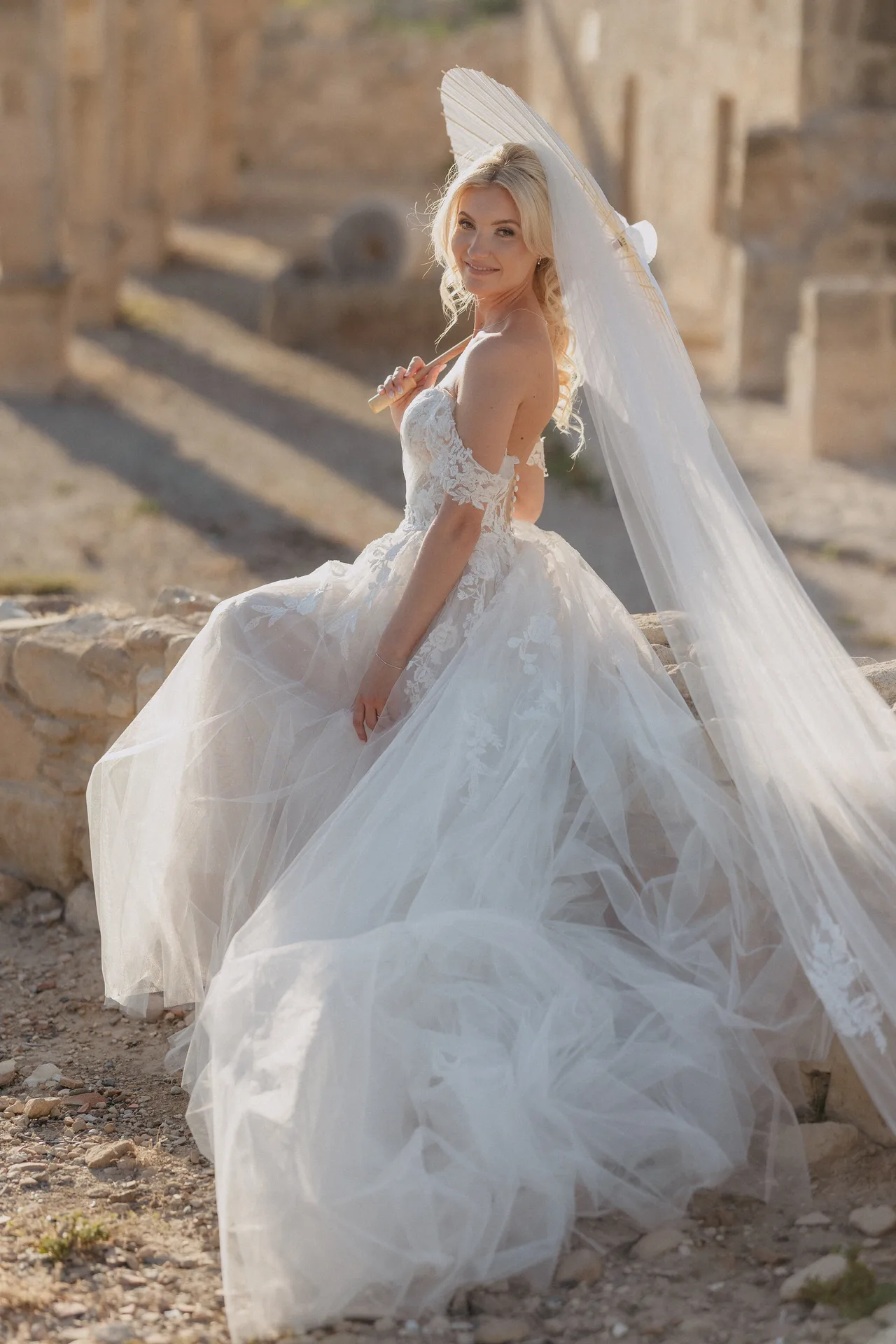 Bride glancing back with a paper parasol among sunlit ancient ruins at Liopetro, Kouklia, Paphos