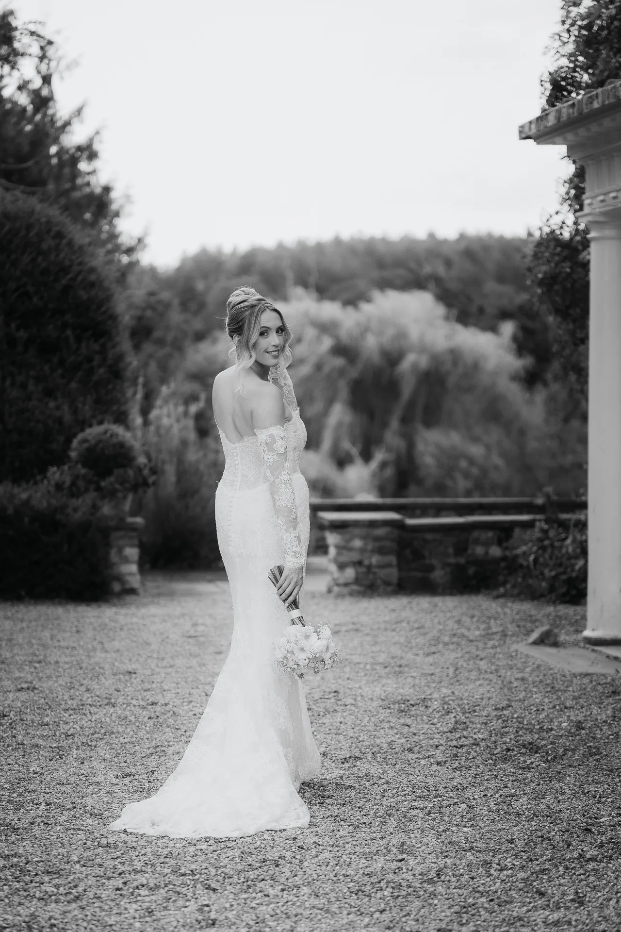 Black-and-white portrait of a bride glancing over her shoulder in the gardens at Northbrook Park, UK