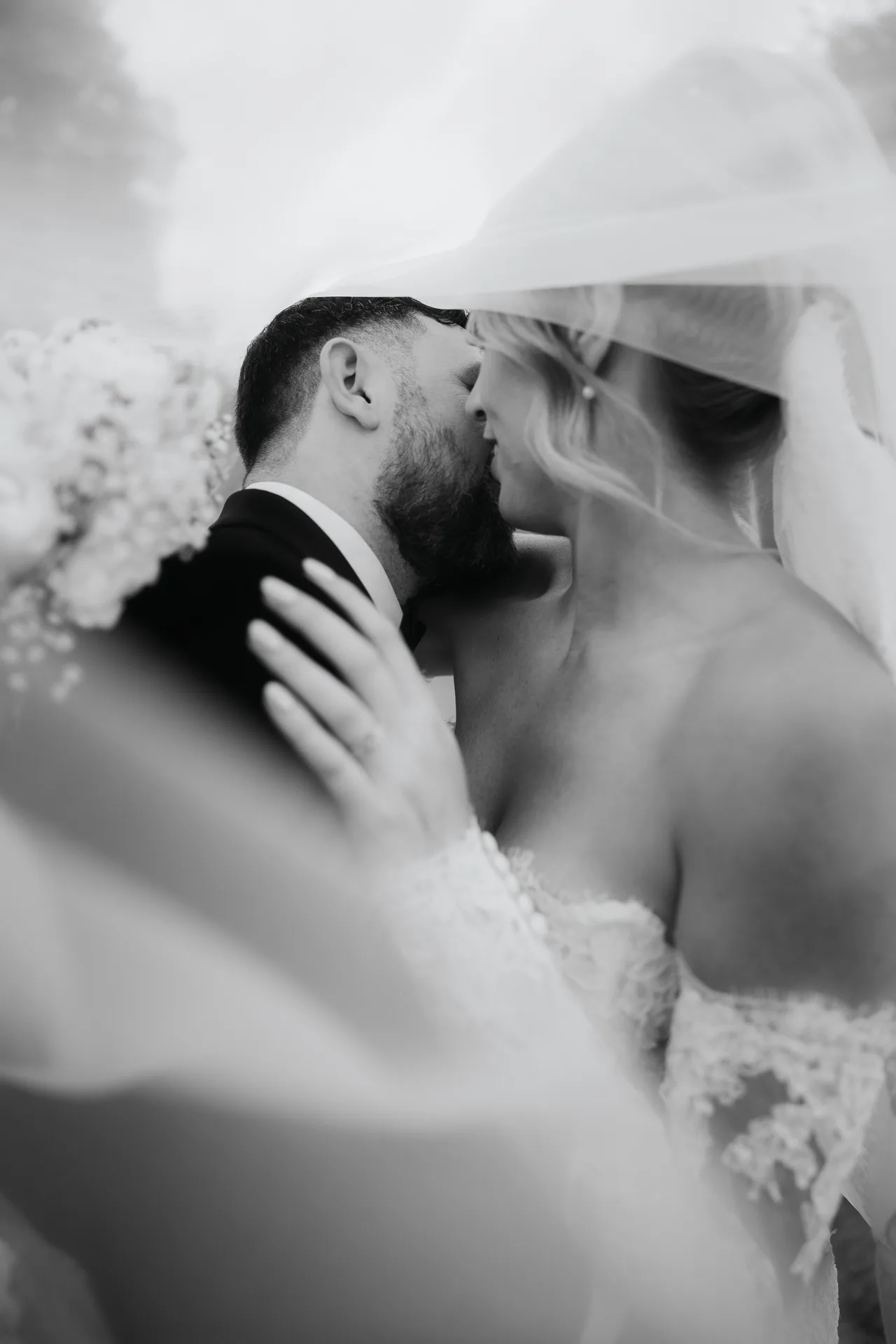 Black-and-white photo of the bride and groom kissing beneath her veil, Northbrook Park, UK