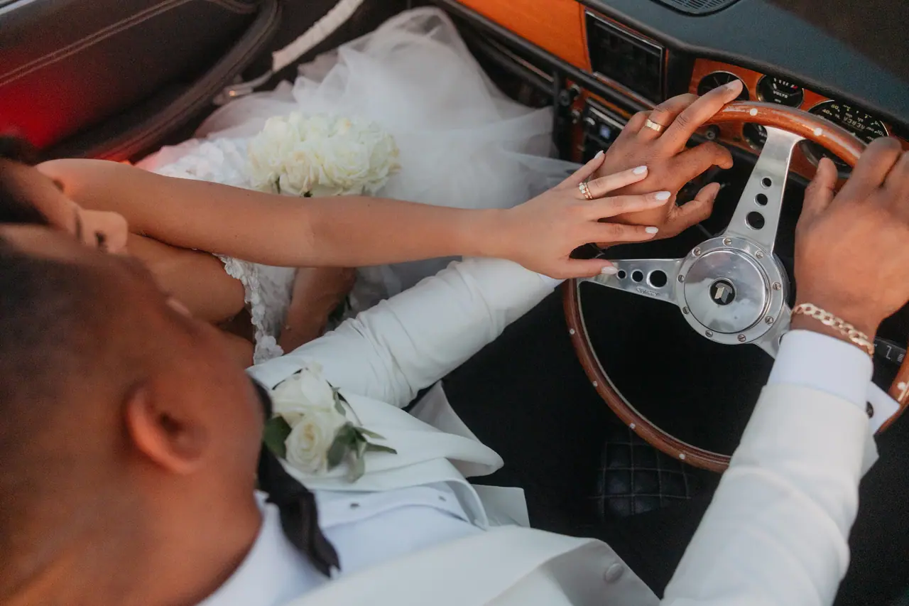 Close-up of the couple's hands on the Triumph Stag's wood-rimmed steering wheel